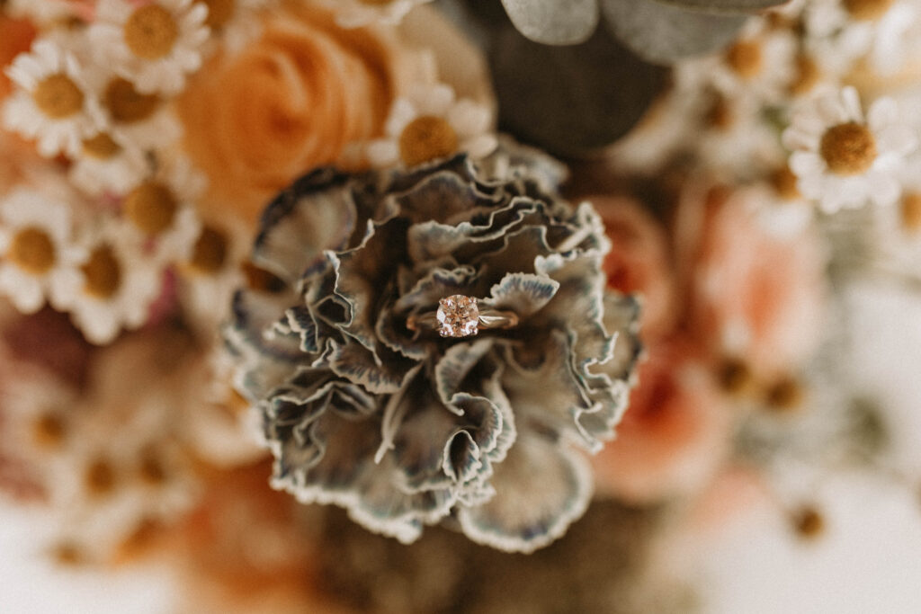 Wedding ring resting on burnt orange, marigold/saffron, rosy brown, and taupe florals.