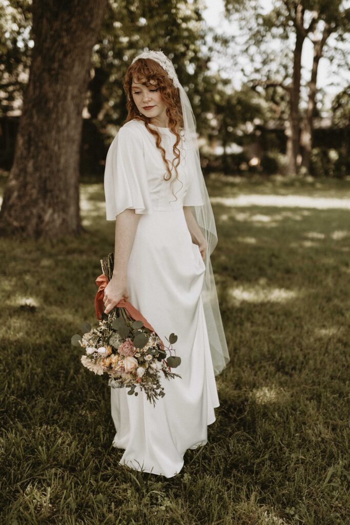 Classy bride wearing a simple, silk gown paired with a vintage veil and a few bling accessories. Her fiery red hair, big blue eyes, and sharp features bring the look to completion.