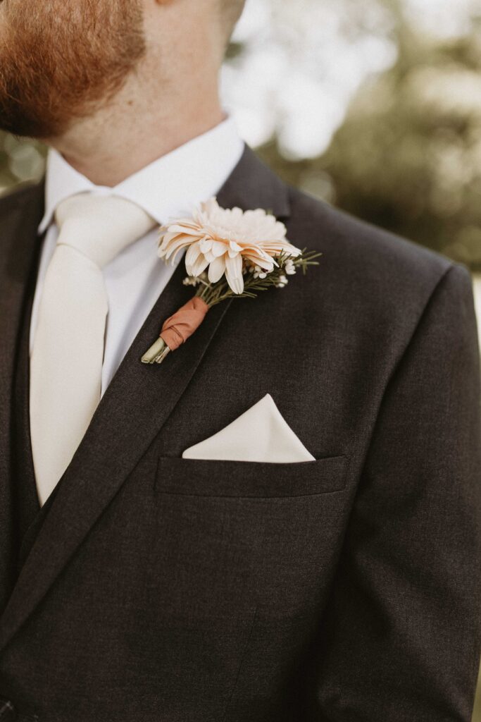 The groom wearing a black suit with brown dress shoes, paired with taupe accents.