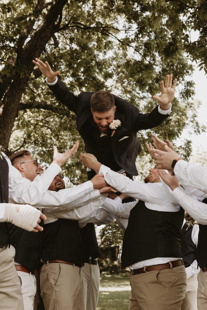 Groomsmen throw the groom in the air.
