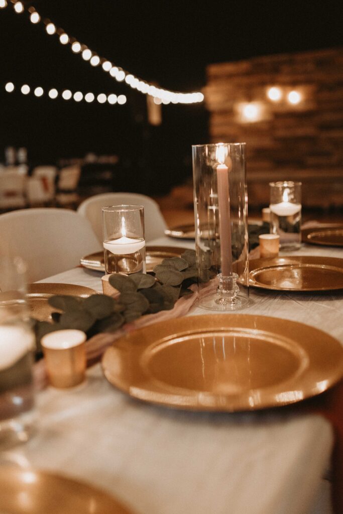 Classy wedding decorations consisting of burnt orange, marigold/saffron, rosy brown, and taupe florals, gold accents, edison lights, and candles.