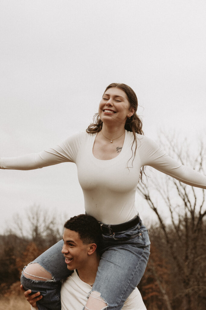 Young girl soars like a bird on top of her boyfriend's shoulders.