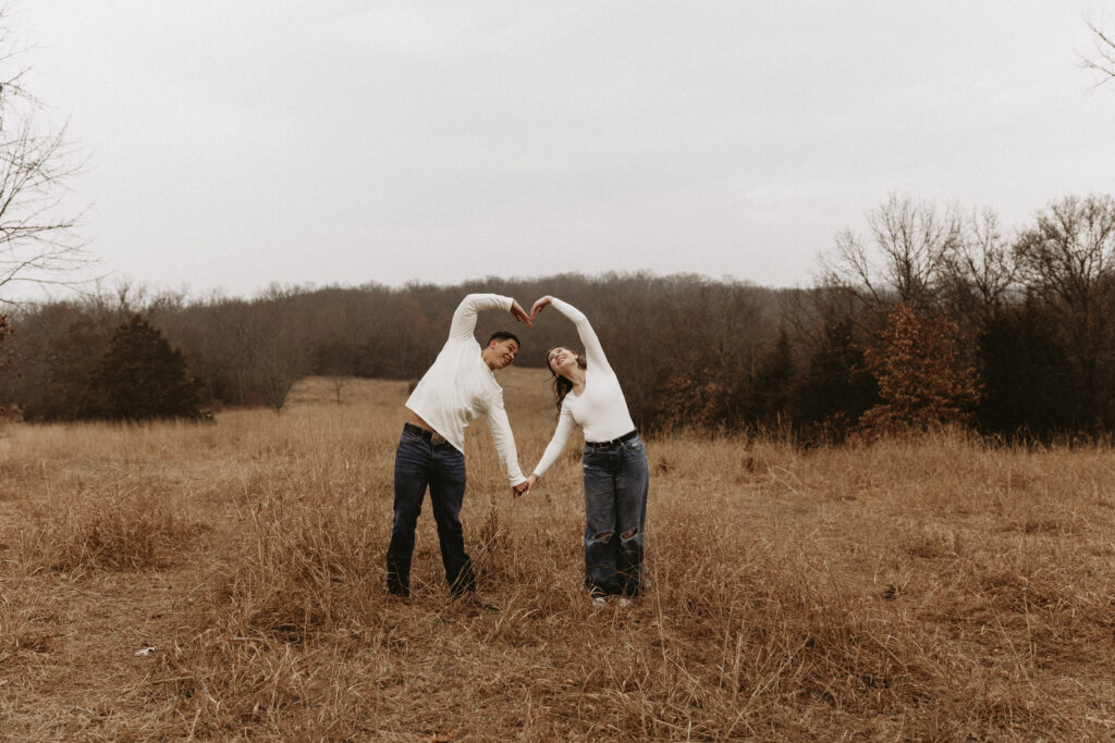 Young couple creates a heart with their hands in an open field.