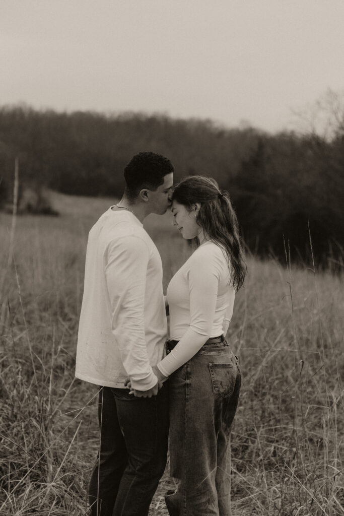 Young man kisses his girlfriend's head in an open field.