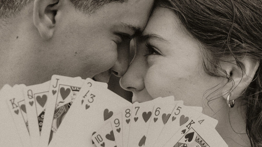 Young couple touch foreheads behind a fan of cards.