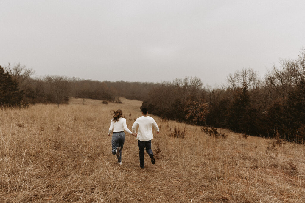 Couple takes hands and runs off into an open field.