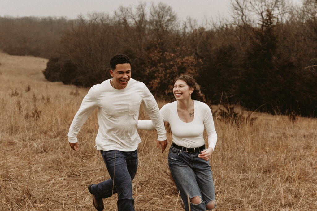 Couple giggles and runs around in an open field.