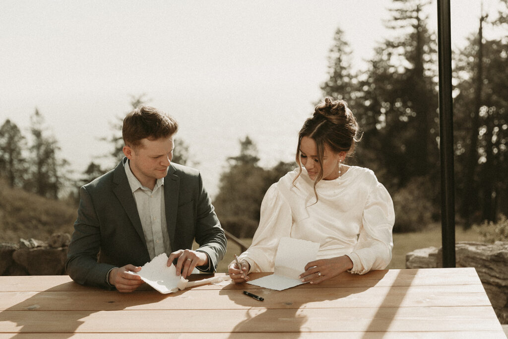 Bride and groom write vows on an outdoor bench table before their dreamy Crook Point elopement in Oregon.