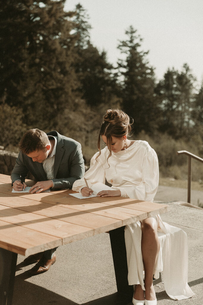 Bride and groom write vows on an outdoor bench table before their dreamy Crook Point elopement in Oregon.
