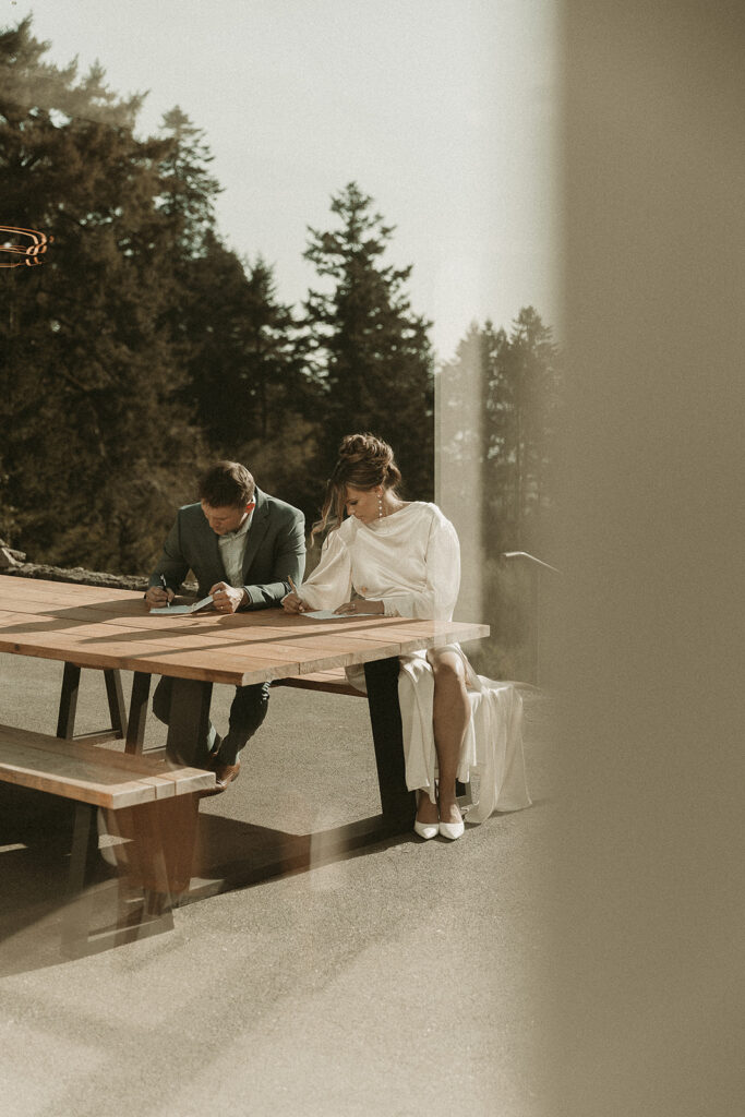 Bride and groom write vows on an outdoor bench table before their dreamy Crook Point elopement in Oregon.