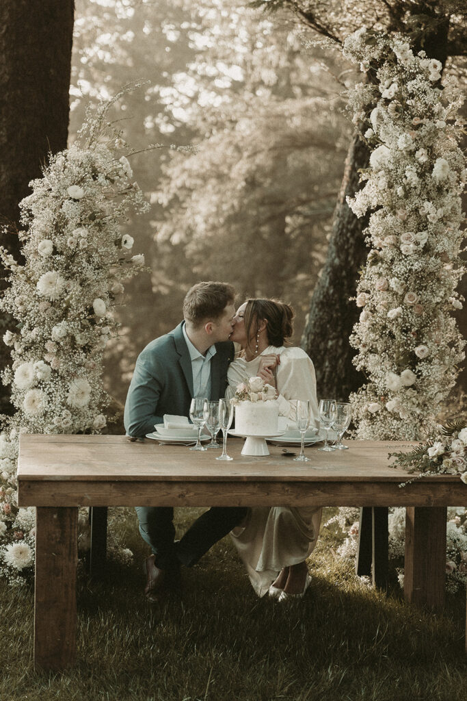 Bride and groom kiss at their dinner table for their dreamy Crook Point elopement in Oregon.