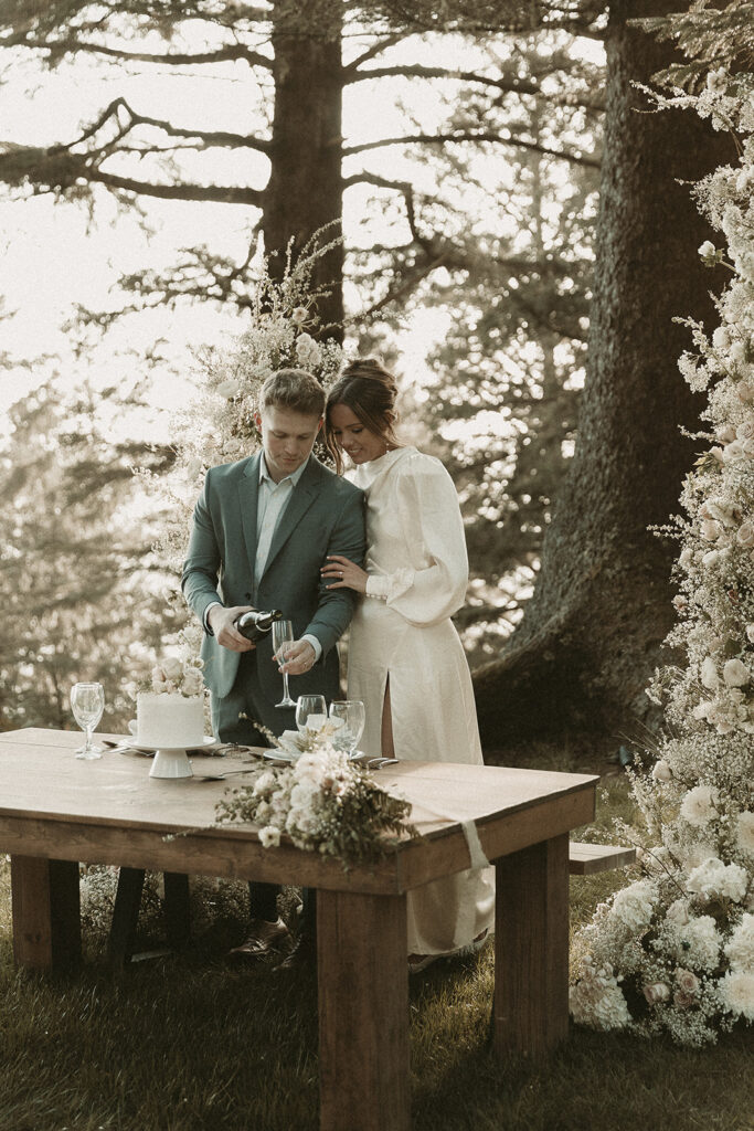 Bride and groom pour champagne at their dinner table for their dreamy Crook Point elopement in Oregon.
