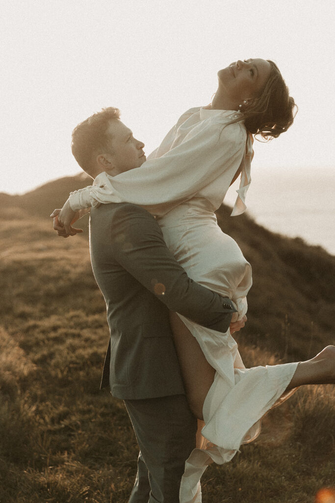 Groom picks bride up during dreamy sunset cliff elopement photos at Crook Point, Oregon.