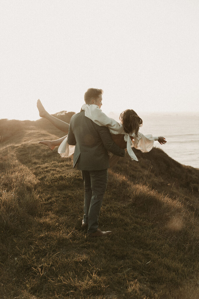Groom picks bride up during dreamy sunset cliff elopement photos at Crook Point, Oregon.
