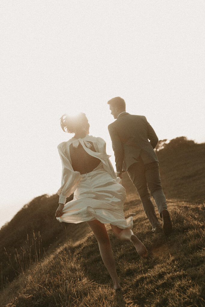 Bride and groom run away from camera during dreamy sunset cliff elopement photos at Crook Point, Oregon.