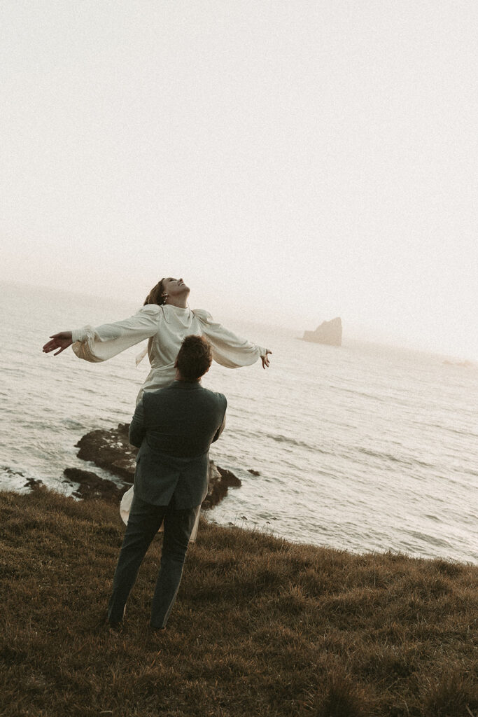 Groom picks bride up and twirls around during dreamy sunset cliff elopement photos at Crook Point, Oregon.