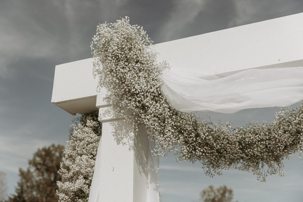 Floral ceremony arch covered in baby’s breath and neutral-toned blooms at The Sycamore Tree venue in Missouri, set in front of the open countryside view.