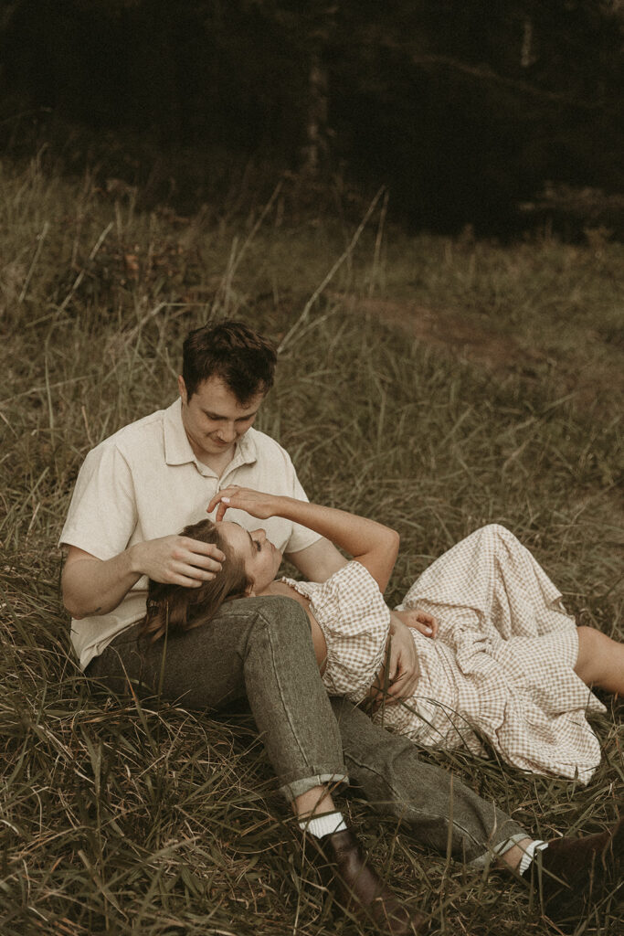 Couple sitting on a grassy bluff at Secret Beach Oregon, cuddling with sea stacks in the background.