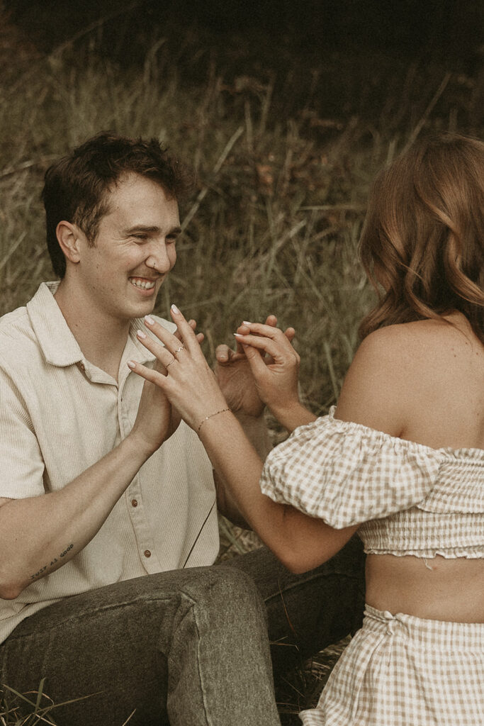 Couple sitting on a grassy bluff at Secret Beach Oregon, cuddling with sea stacks in the background.