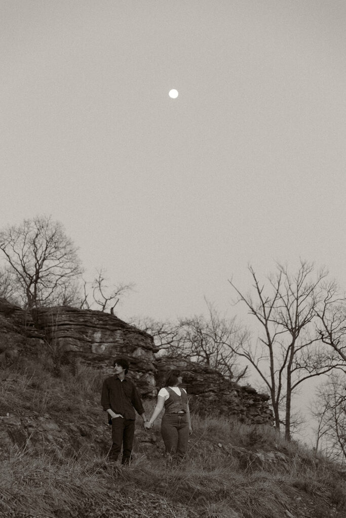 Young couple hold hands under the moon atop of a bluff for their engagement session in Kansas City, MO.