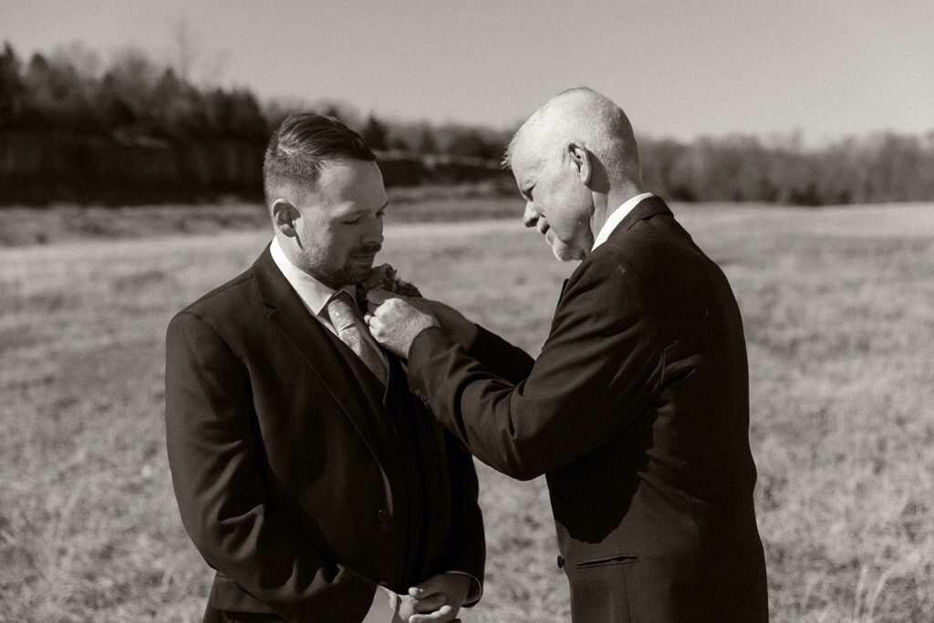 Spring micro wedding at Blue Springs Lake, Missouri. Father pins boutonniere on groom.